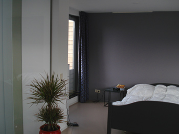 Warm grijs op de muur achter het bed en een greige vloer: kleur ideeën voor in de slaapkamer
